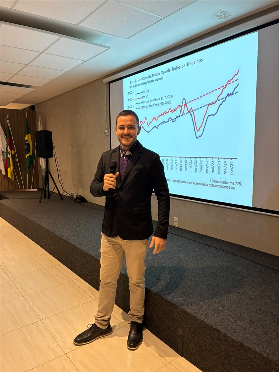 Leonardo Lauxen de microfone na mão em auditório com telão de indicadores